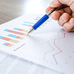 Hand pointing to coloured graphs on paper.